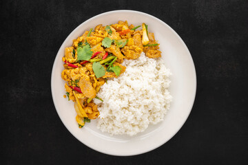 Stir Fried Chicken with Curry Powder beside Steamed Rice in simply white ceramic plate on dark tone texture background, top view, Gai Pad Pong Karee, Thai food