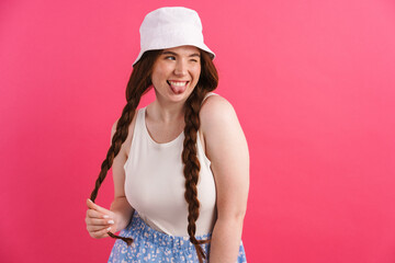 Naklejka premium Young ginger woman showing her tongue while holding her pigtail