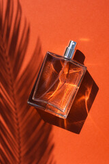 Transparent bottle of perfume on a terracotta color background. Fragrance presentation with...