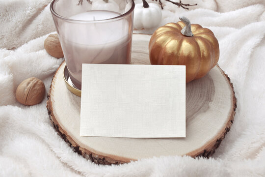 Close fall or winter composition with empty blank invitation, decor pumpkin and aroma candle on cosy plaid.  Walnuts. Minimalist mockup scene for autumn wedding, Thanksgiving. Eco home concept.