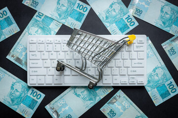 Brazilian money, White computer keyboard, Miniature shopping cart, Black background, Online...