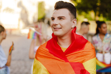 White man smiling and holding rainbow flag during pride parade at city