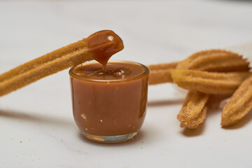 Traditional churros with sugar and cinnamon served on a marble table, with a bowl of caramel.