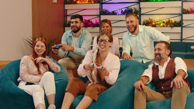 A small group of people are in a warm lighting room as they are sitting down and feeling very joyful playing video games