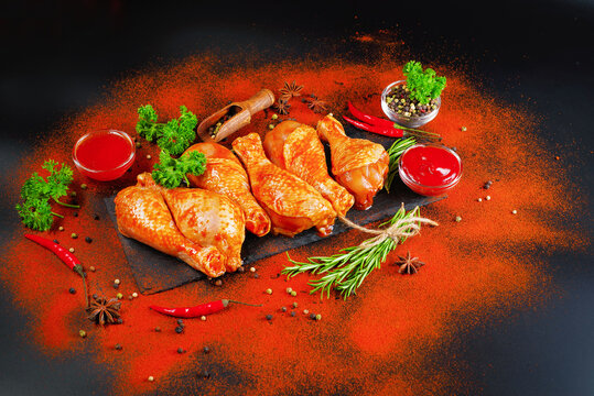 Barbecue marinated chicken dramstik on a black cooking board, with fresh rosemary leaves and fresh cherry tomatoes and various spices, close-up.Semi-finished product, Marinated product, quick cooking.