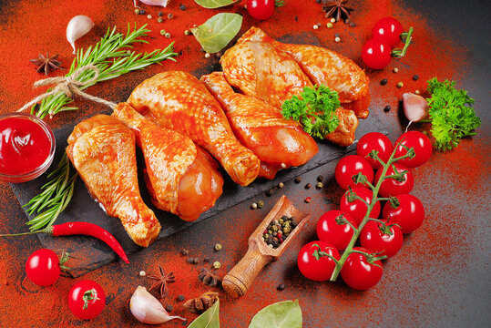 Barbecue marinated chicken dramstik on a black cooking board, with fresh rosemary leaves and fresh cherry tomatoes and various spices, close-up.Semi-finished product, Marinated product, quick cooking.