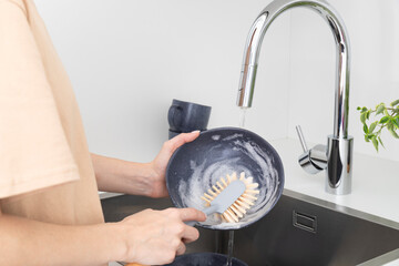 Young woman washes dishes with brush with natural bristles in kitchen. Zero waste concept.