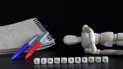 Word linguistics next to a notepad, a fountain pen and a wooden anthropomorphic mannequin. The...