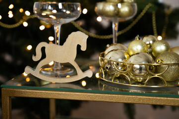 Christmas Tree on background. New Year's or Christmas table, champagne glasses, wooden horse toy and golden balls