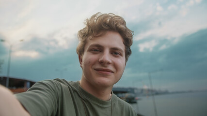 Fototapeta premium Young blond boy making video call and waving hand he say hello on amazing sunset cloudy background
