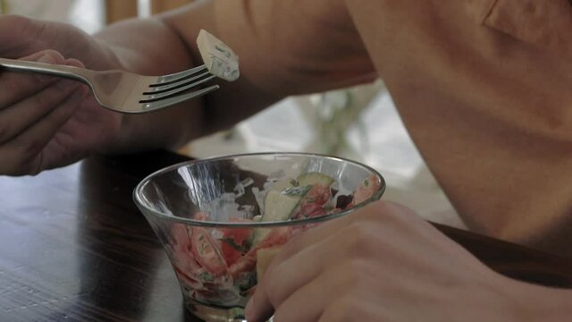 Close-up of a man with an appetite eating a vegetable salad from a small glass plate.