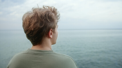 Fototapeta premium Young handsome blond boy puts his hands behind his neck and looks towards the horizon, deep in thought