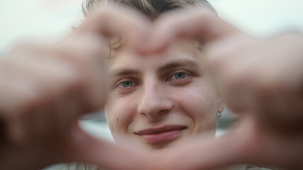 Blond boy towards camera making heart symbol with hand and smiling looking at camera close-up