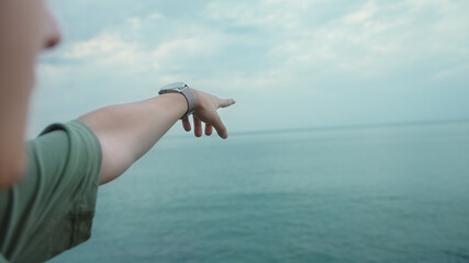 Young man pointing to the horizon with his forefinger while looking out to sea