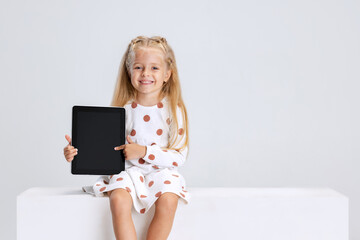 Portrait of little preschool girl pointing at tablet isolated over white studio background.