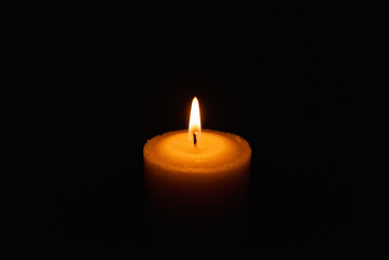 One single light candle burning brightly in the black background.Spiritual candle yellow flame. Flame of candle in the darkness.Copy space.