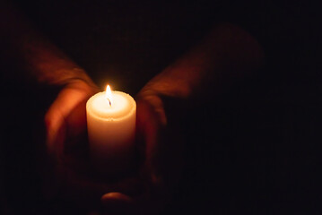 Hands holding burning candle in dark like a heart.Selective focus,black background.Copy space.