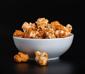 Sweet popcorn with caramel syrup in a white ceramic bowl on a glossy black background with reflection
