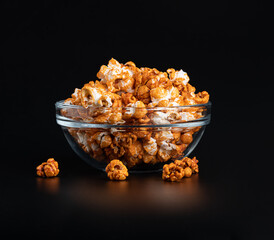 Sweet popcorn with caramel syrup in a transparent bowl on a glossy black background with reflection