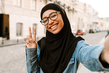 Young muslim woman wearing hijab gesturing while taking selfie photo