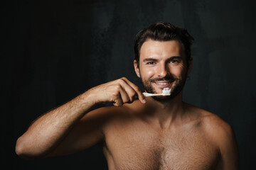 Young half-naked man smiling while brushing his teeth