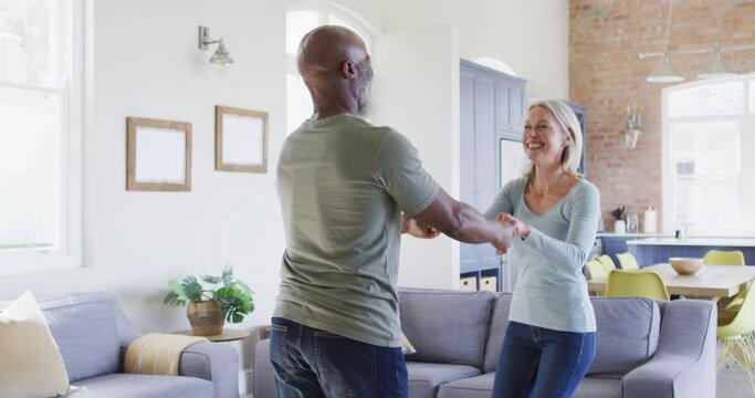 Mixed race senior couple dancing together in the living room at home