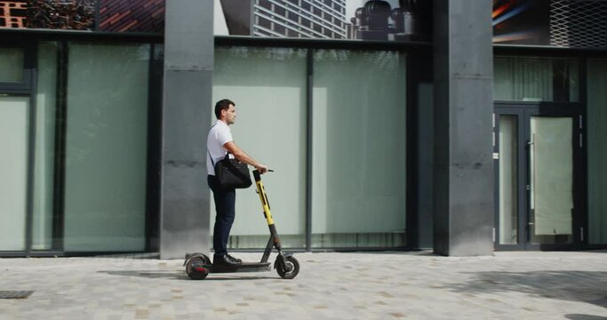 Side view of businessman riding electric scooter along pathway. Handsome confident young man riding electric scooter on urban city street