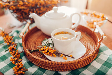 Obraz na płótnie Canvas Tea with sea buckthorn berries served in cup and kettle on tray. Healthy hot drink for cold fall and winter days