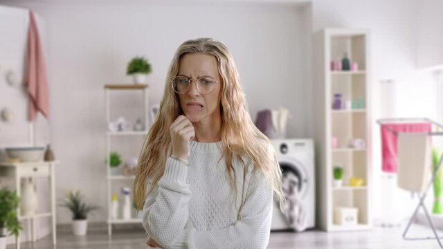 Hmm. Suspicious thoughtful young female looking up, keeping hand on her face as if trying hard to remember something important. A confused woman at home on a room background