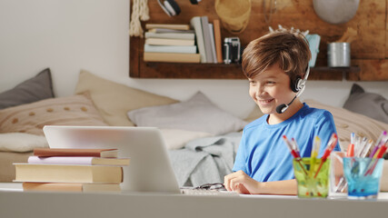 smiling student boy studying on the computer at remote school on the web, concept of browsing and searching the internet or other activities such as social media or online games or entertainment