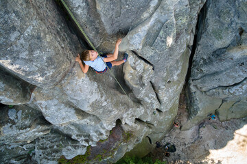 Young child boy climbing steep wall of rocky mountain. Kid climber overcomes challenging route. Engaging in extreme sport concept.