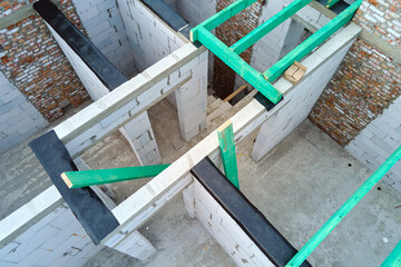 Aerial view of unfinished frame of private house with aerated lightweight concrete walls and wooden roof beams under construction.