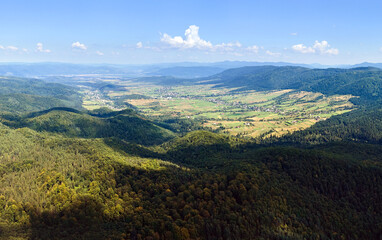 Aerial view of mountain hills covered with dense green lush woods on bright summer day.