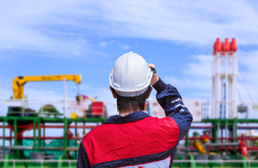 Rear view of young engineer in blue mechanic jumpsuit wearing white safety helmet before working on oil tanker ship at shipyard