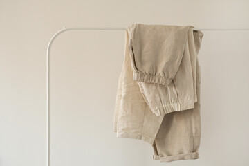 Minimal aesthetic fashion clothes concept. Washed linen female pants and trousers on hanger on white background. Fashion blog, website, social media - obrazy, fototapety, plakaty