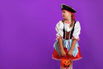 Little girl in a carnival costume of a pirate for Halloween on a purple background. The child looks...
