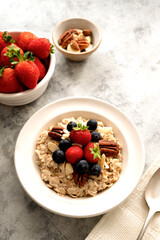 Oatmeal porridge with fresh berries blueberry and strawberries in white bowl on grey background.