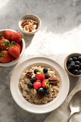Oatmeal porridge with fresh berries blueberry and strawberries in white bowl on grey background.