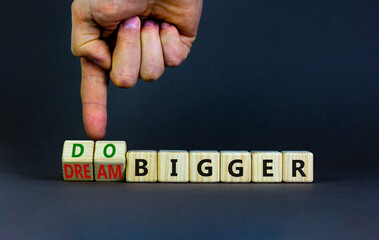 Dream and do bigger symbol. Businessman turns wooden cubes and changes words dream bigger to do...