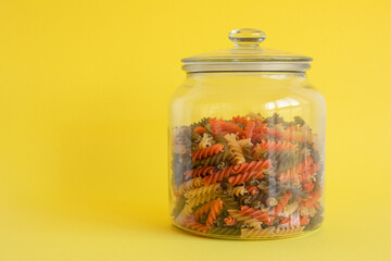 Glass jar filled with colorful spiral pasta isolated on yellow background