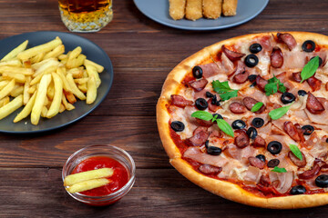 Pizza on a platter close-up on the table with ketchup, juice, sauce and potatoes on a dark wooden table in the rustic style.