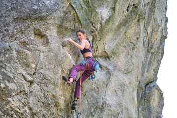 Strong female climber climbing steep wall of rocky mountain. Sportswoman overcoming difficult...