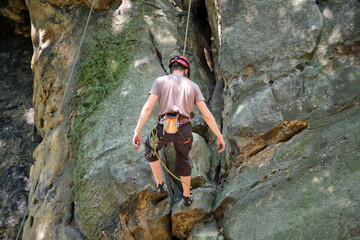 Young man climbing steep wall of rocky mountain. Male climber overcomes challenging route. Engaging...