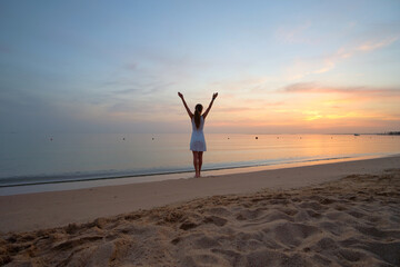 Fototapeta na wymiar Young happy woman standing on sandy beach by seaside enjoying warm tropical evening.