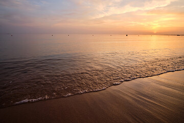 Calm sea shore with crushing waves on sandy beach at sunrise.