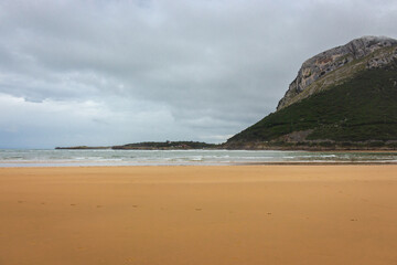 Wide surf beach with mountain in clouds. Autumn landscape with empty coastline. Turquoise seascape. Camino de Santiago landscape. Tourism in Spain. Travel inspiration concept. Beauty in coastal nature