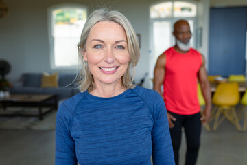 Portrait of happy senior diverse couple in exercise clothes practicing yoga, looking at camera