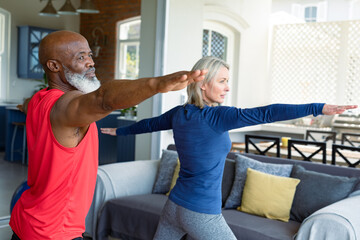 Happy senior diverse couple in exercise clothes practicing yoga together, stretching