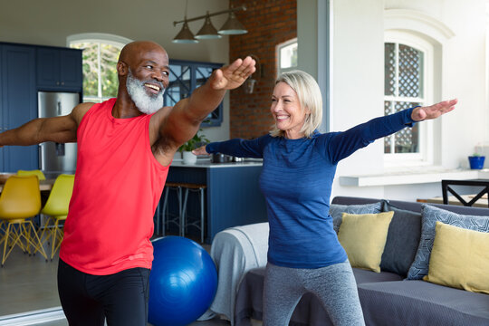 Happy senior diverse couple in exercise clothes practicing yoga together, stretching