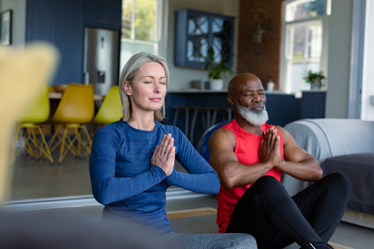 Happy senior diverse couple in exercise clothes practicing yoga together, meditating
